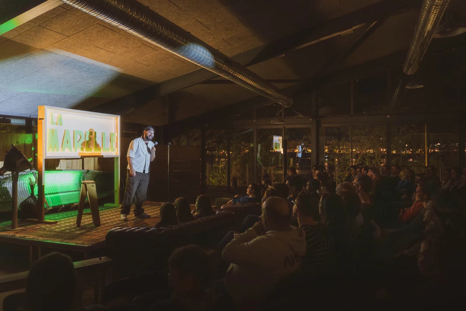 Humoriste sur scène à La Marelle Verte — comedy club en plein air aux Chantiers de la Garonne, Bordeaux, le mercredi